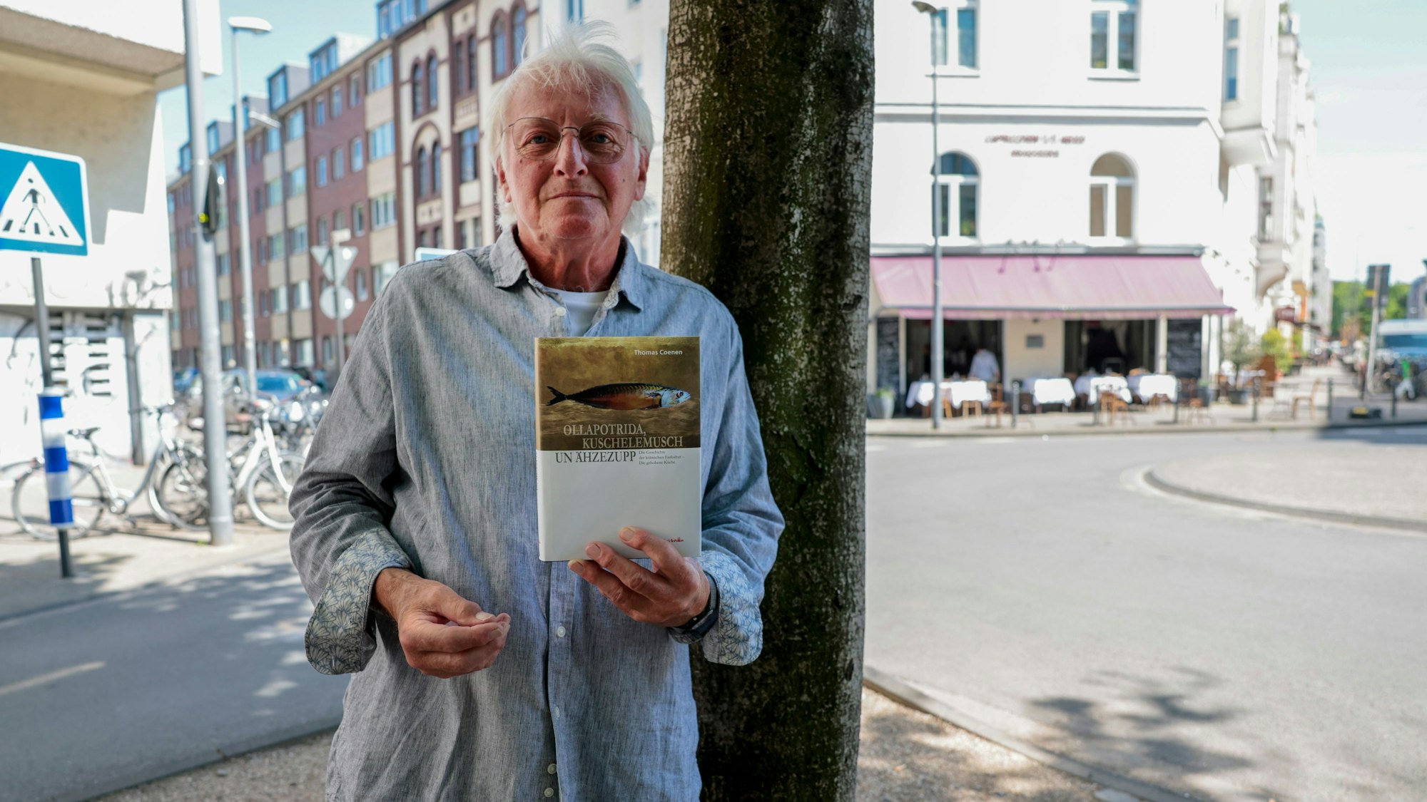 Das Bild zeigt den Autor mit seinem Buch in der Hand vor einem Baum und dem Restaurant in der Südstadt.