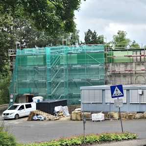 Blick auf die eingerüstete Turnhalle. Im Hintergrund ist ein Kran zu sehen.