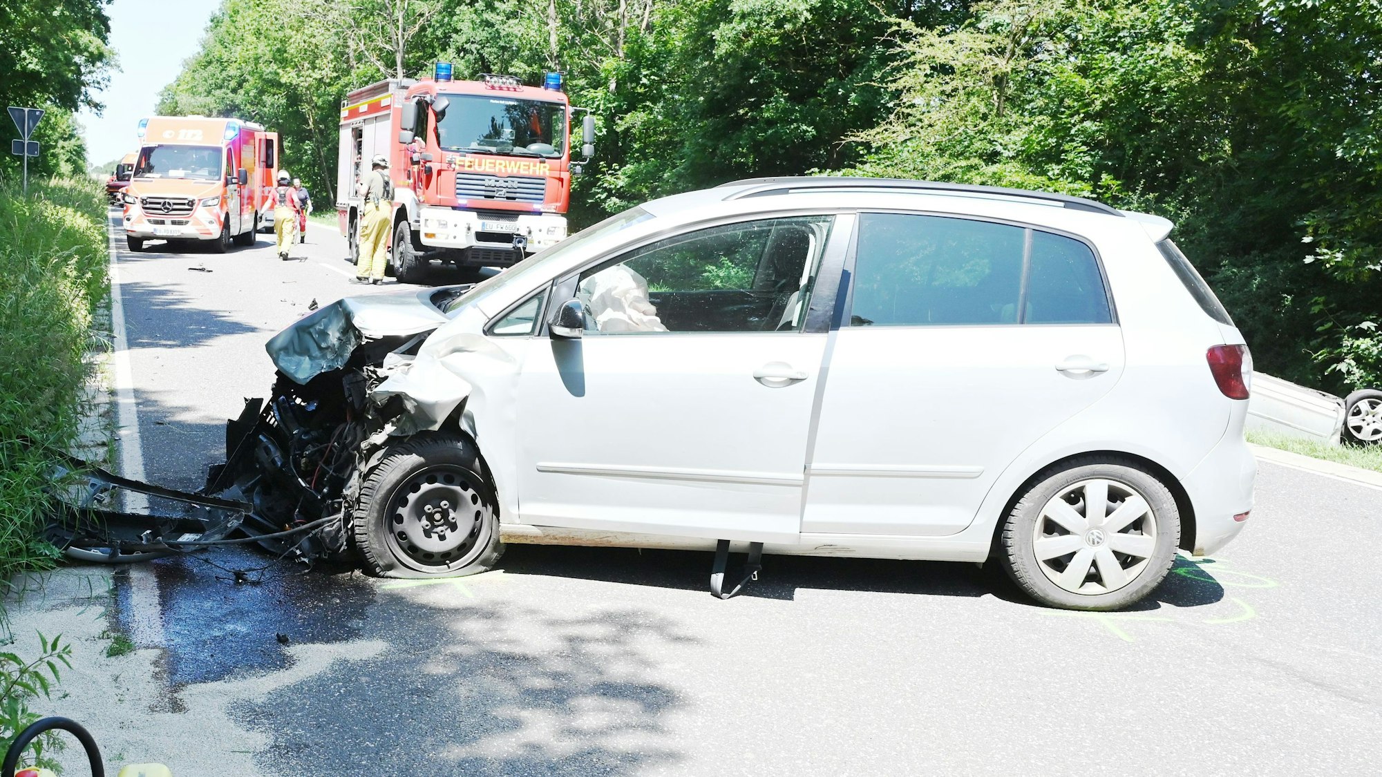 Das Bild zeigt ein stark beschädigtes Auto, im Hintergrund Fahrzeuge von Rettungsdienst und Feuerwehr.