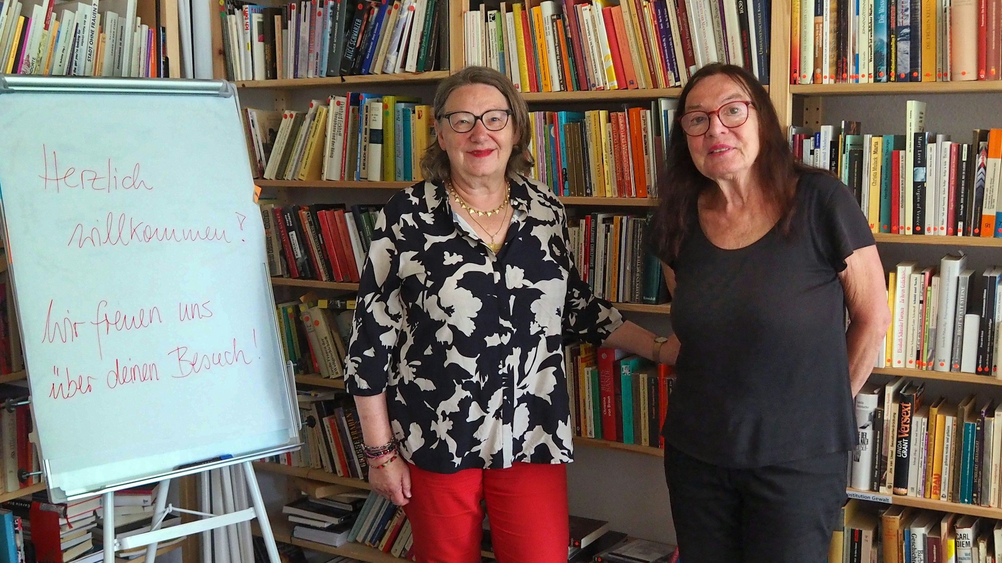 Zwei Frauen stehen vor einer Regalwand mit Büchern.