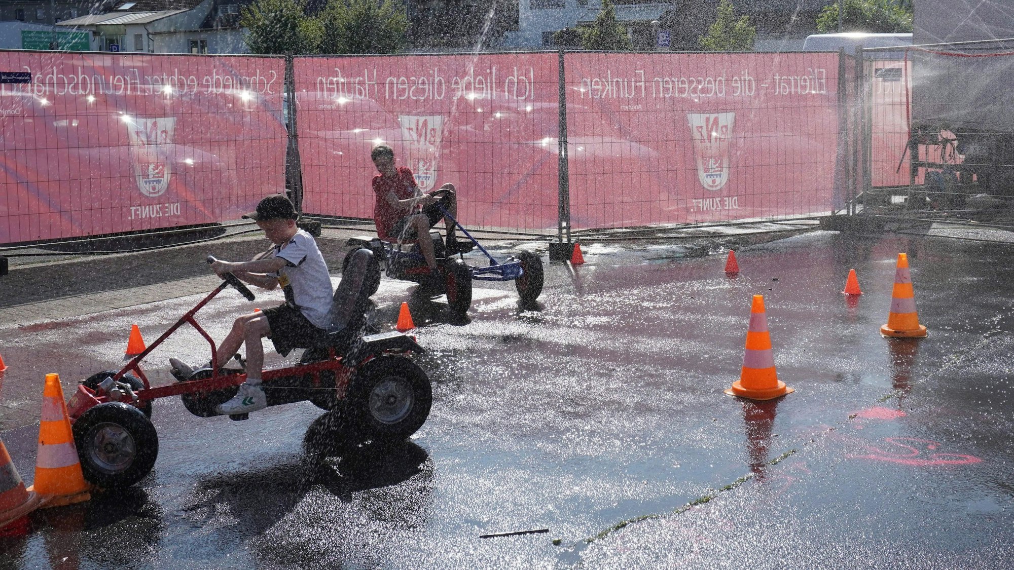 Auf dem Bild sind zwei Jungen zu sehen, die in einem Gokart durch einen Wasserparcours fahren.