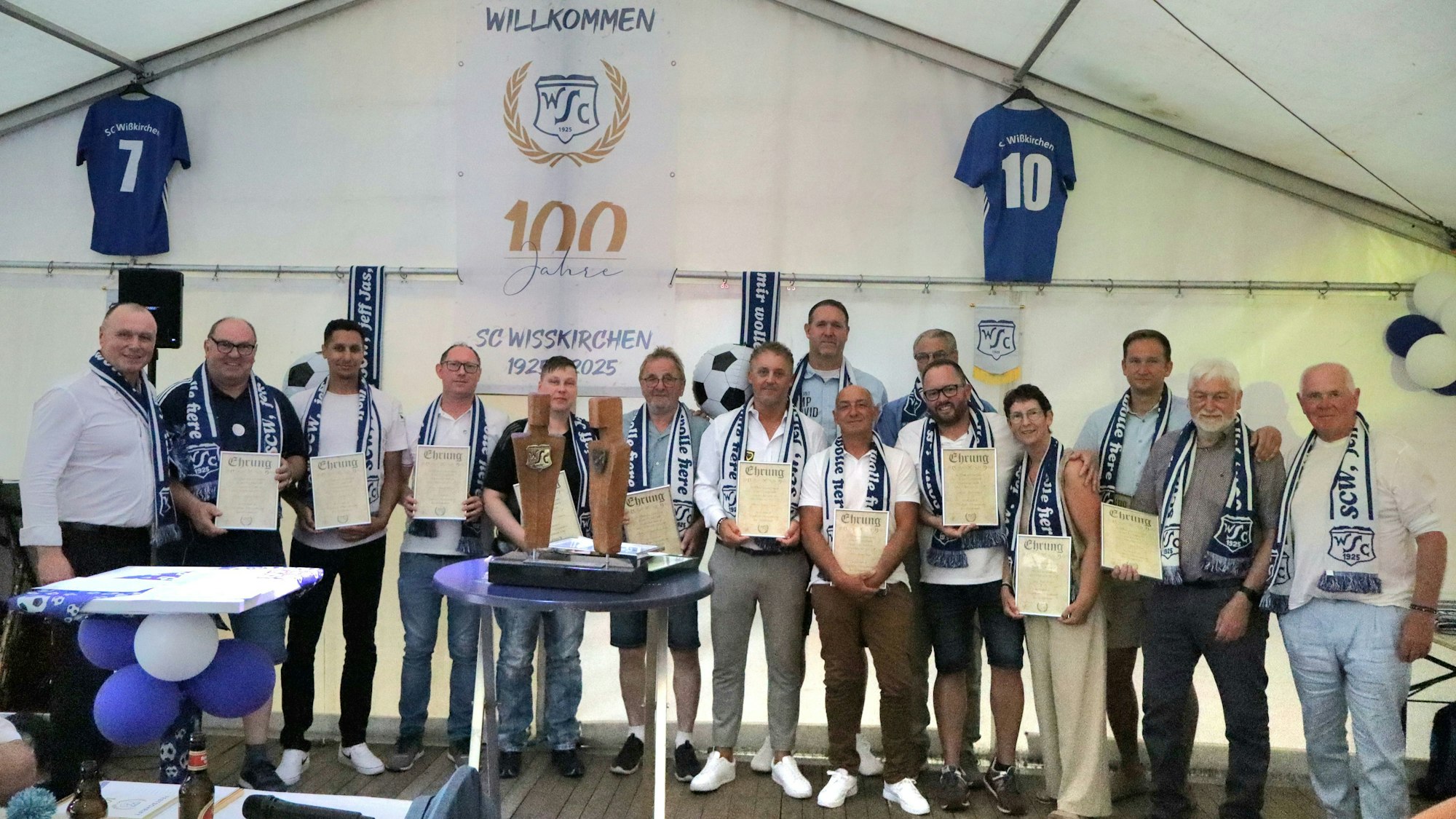 Das Bild zeigt die ausgezeichneten Vereinsmitglieder mit ihren Ehrenurkunden. Sie stehen nebeneinander in einem Festzelt.