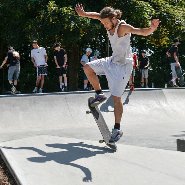 Zu sehen ist ein junger Mann, der einen Trick mit seinem Skateboard versucht.