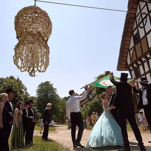 Das Bild zeigt das Maikönigspaar tanzend vor einem historischen Gebäude. Die Eierkrone hängt über den beiden in der Luft.