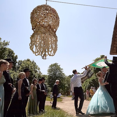Das Bild zeigt das Maikönigspaar tanzend vor einem historischen Gebäude. Die Eierkrone hängt über den beiden in der Luft.