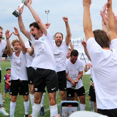 FlaKi-Kapitän Lukas Mager reckt den Pokal in die Höhe. Er und seine Mitspieler jubeln.
