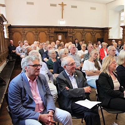 Das Bild zeigt die Teilnehmerinnen und Teilnehmer während der Feier in einem Raum mit Holzvertäfelung an den Wänden.