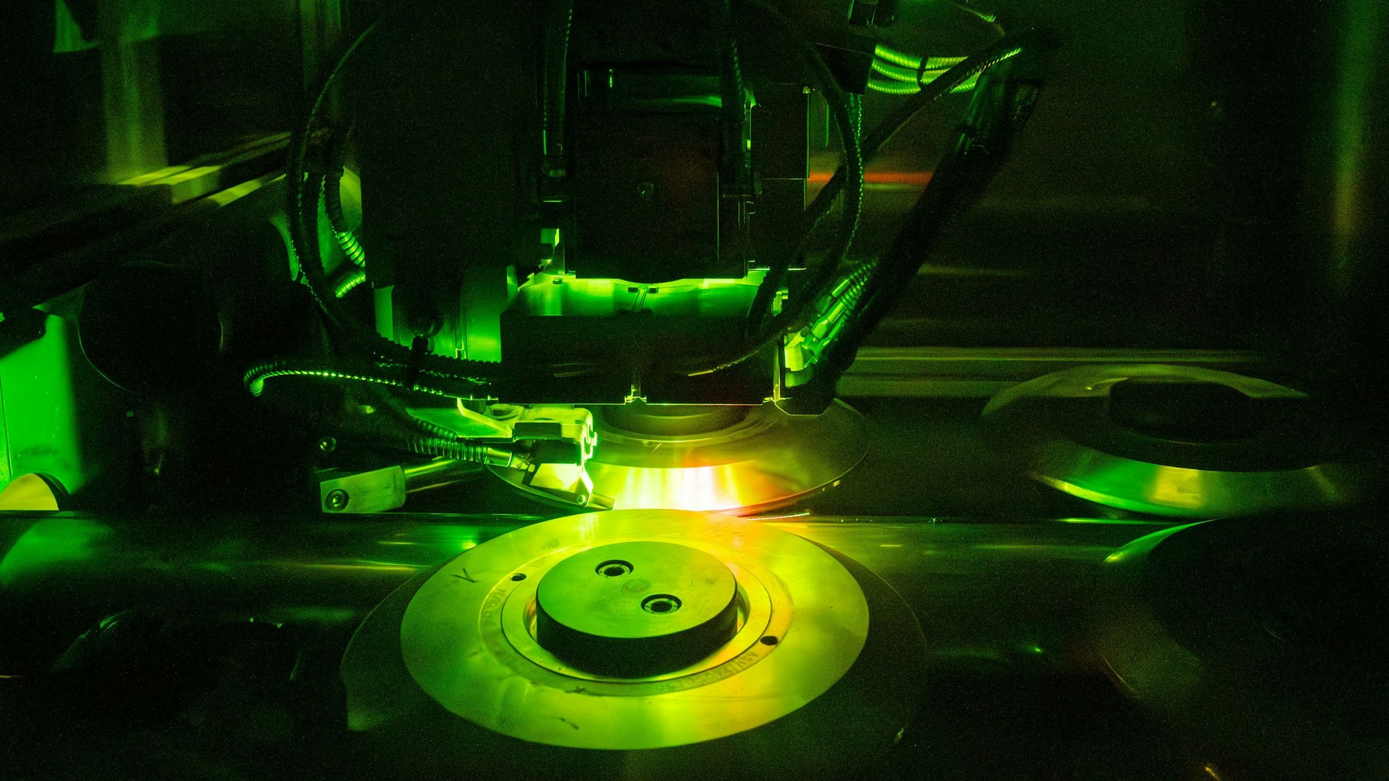 In grünem Licht ist hinter Schutzglas ein Schweißprozess in einem Industriebetrieb zu beobachten.