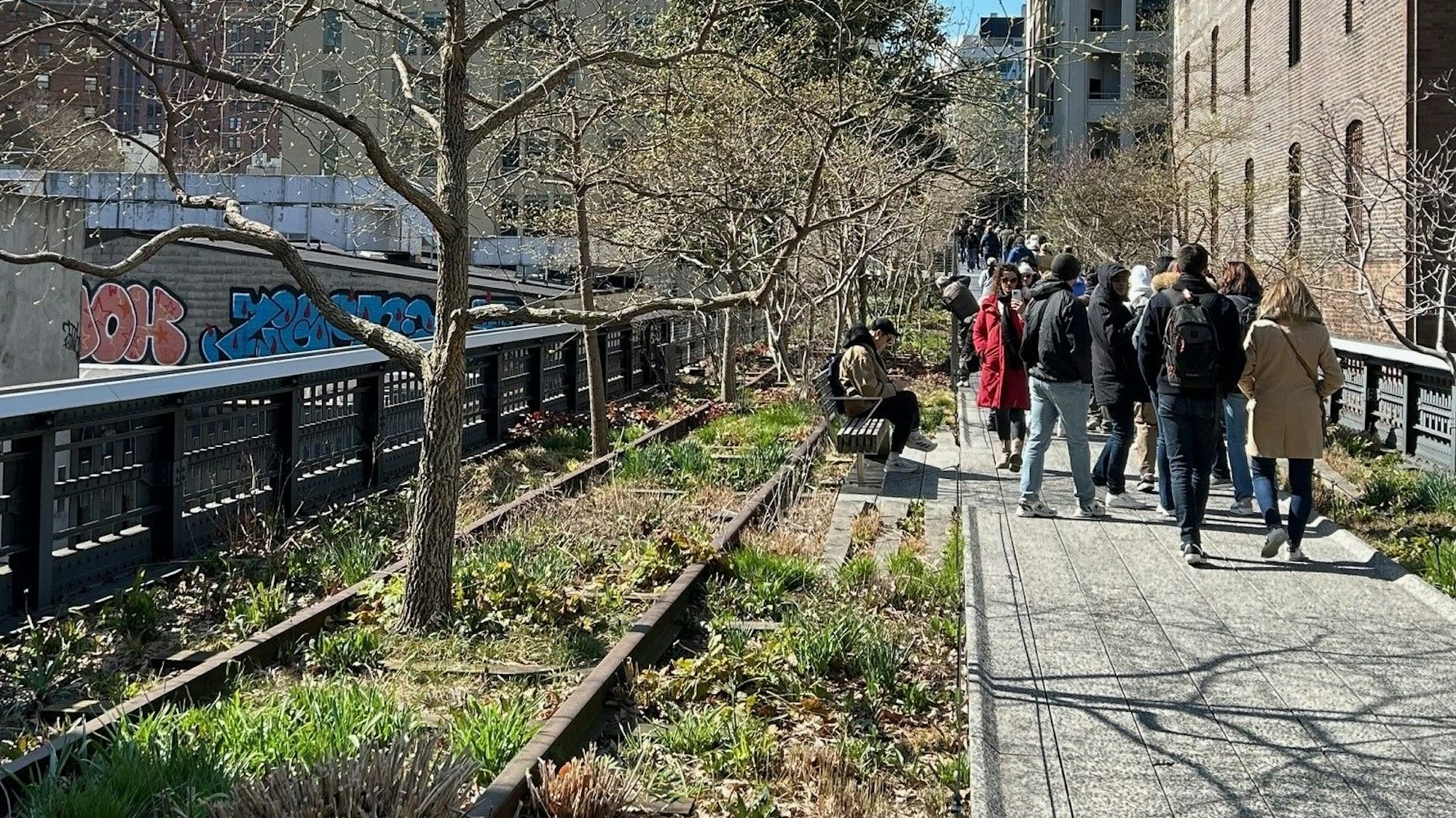 Auf einem von einem Geländer eingefassten Fußweg mit Begrünung sind Menschen unterwegs.