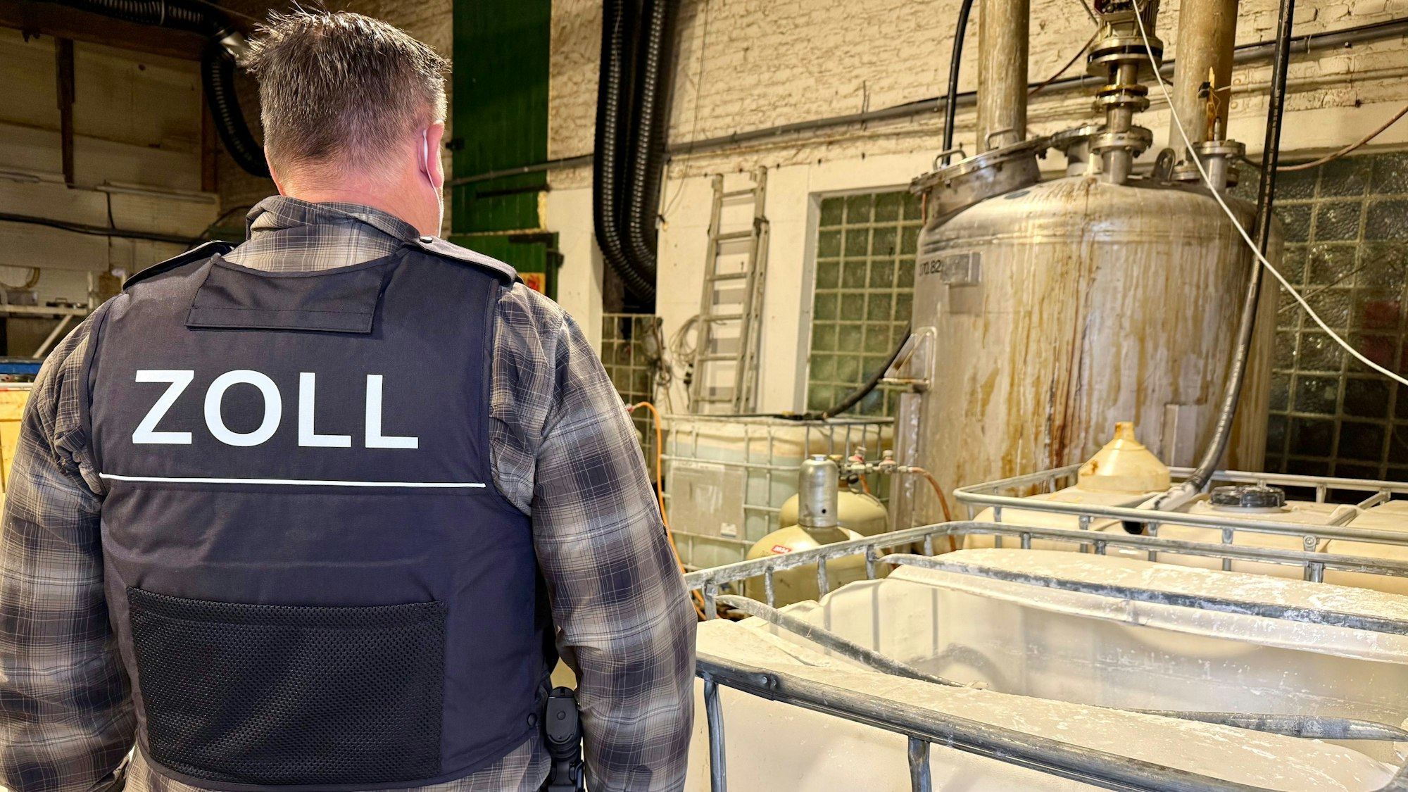Das Bild zeigt einen Zollbeamten auf einer Hofanlage in Kerpen, wo illegal Drogen hergestellt wurden.