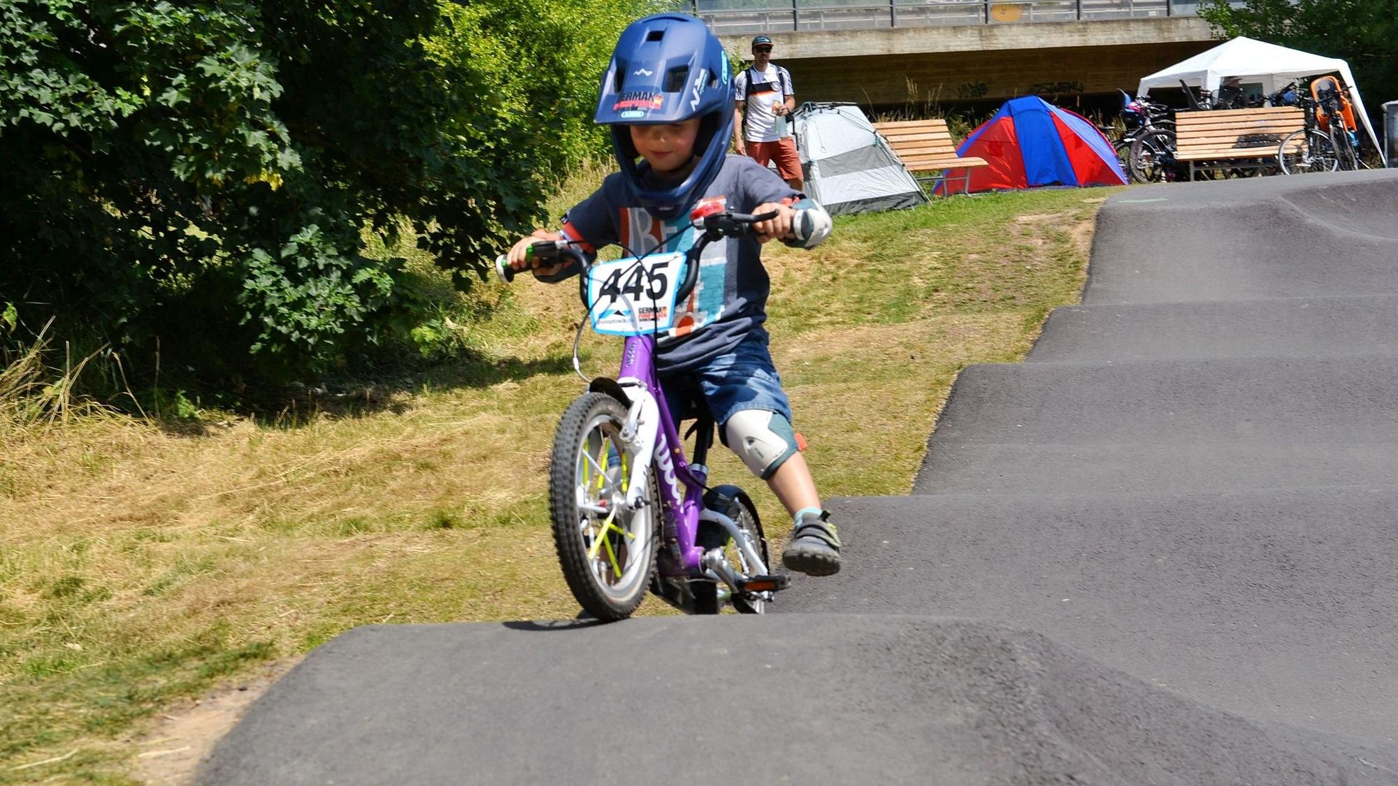 Ein kleiner Junge trägt Helm und Knieschoner, als er mit einem Fahrrad über den Pumptrack in Weilerswist fährt.