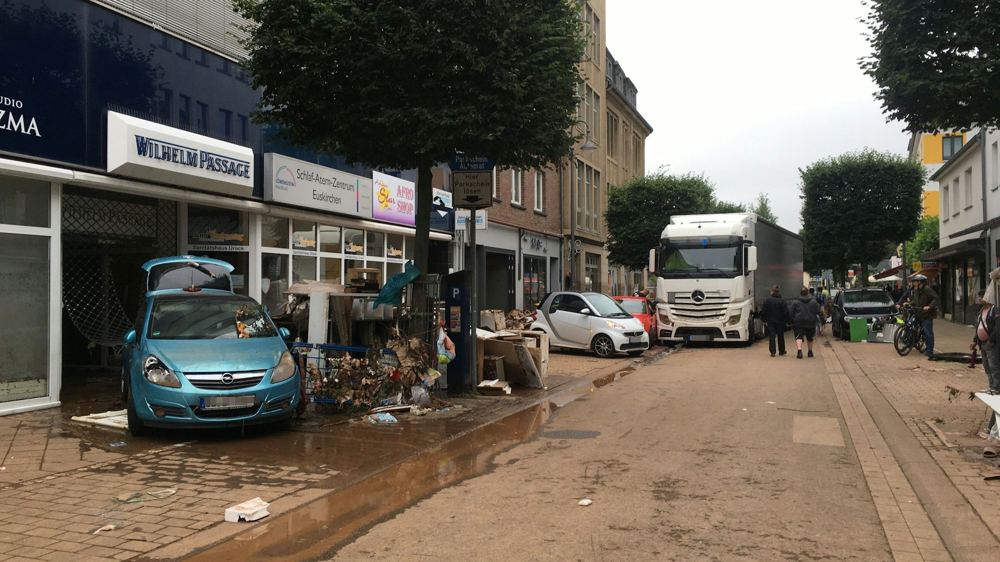 Das Bild zeigt eine von Schlamm überzogene Fahrbahn, Sperrmüll sowie Autos und einen Lastwagen, die von den Fluten mitgerissen wurden.