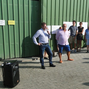 Mehrere Menschen stehen im Halbkreis vor einer großen Halle mit grüner Wand.