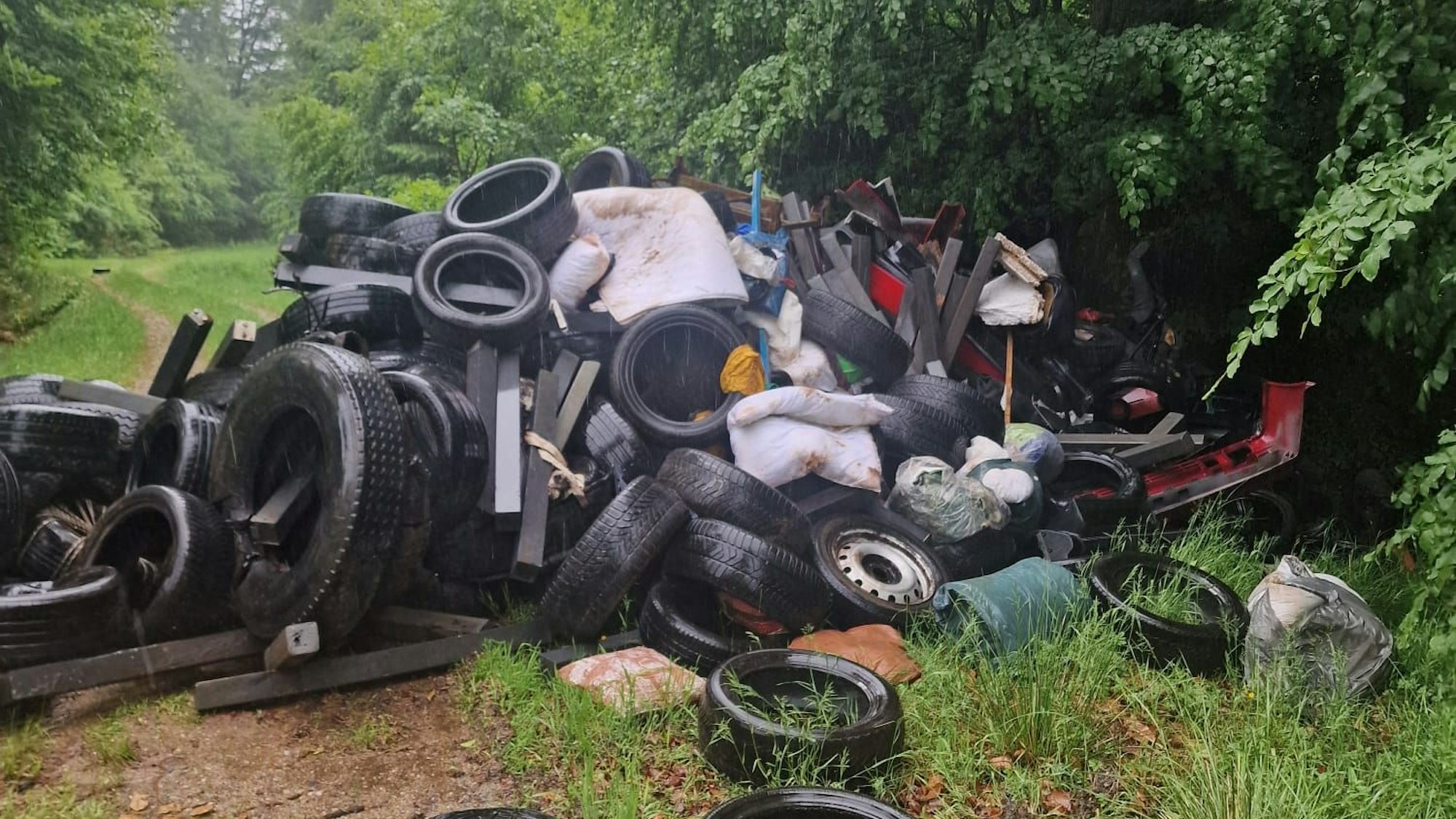 Auf einem Waldweg liegt ein großer Berg aus Sperrmüll, Altreifen und Autoteilen.