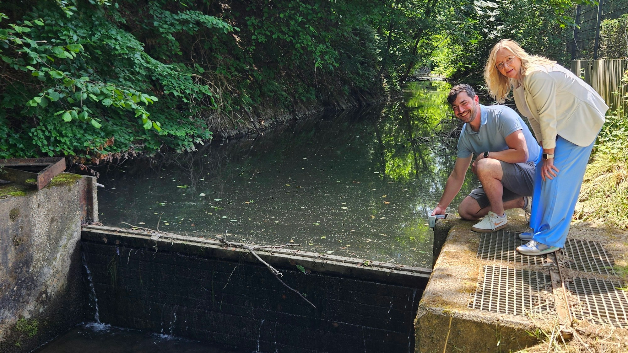 Thomas Scholzen kniet neben dem Wehr, Sabine Preiser-Marian steht daneben.
