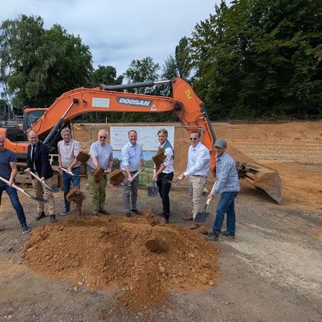 Das Foto zeigt eine Gruppe von Männern beim symbolischen Spatenstich auf der Baustelle in der ehemaligen Radrennbahn.