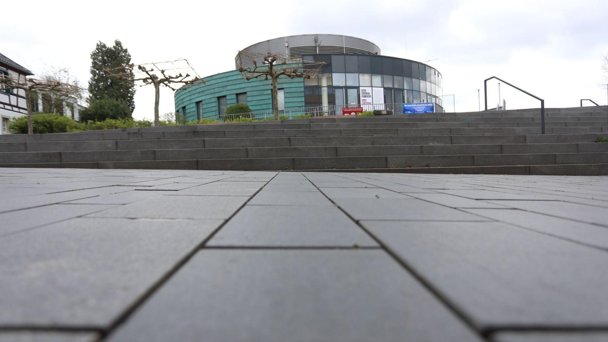 Ein Vorplatz und Treppenstufen vor einem ovalen Gebäude.
