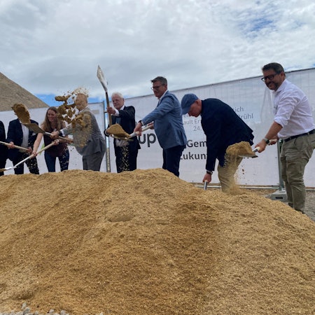 Zu sehen sind Männer und eine Frau, die mit Spaten Sand schaufeln.
