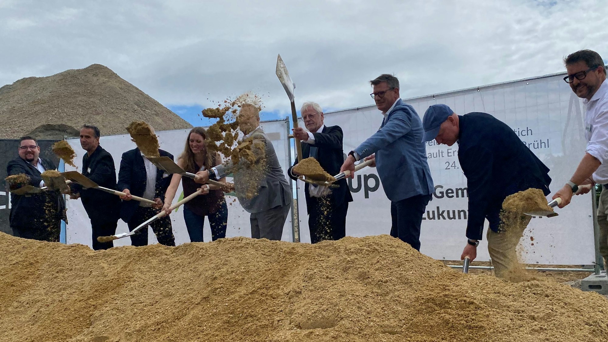 Zu sehen sind Männer und eine Frau, die mit Spaten Sand schaufeln.