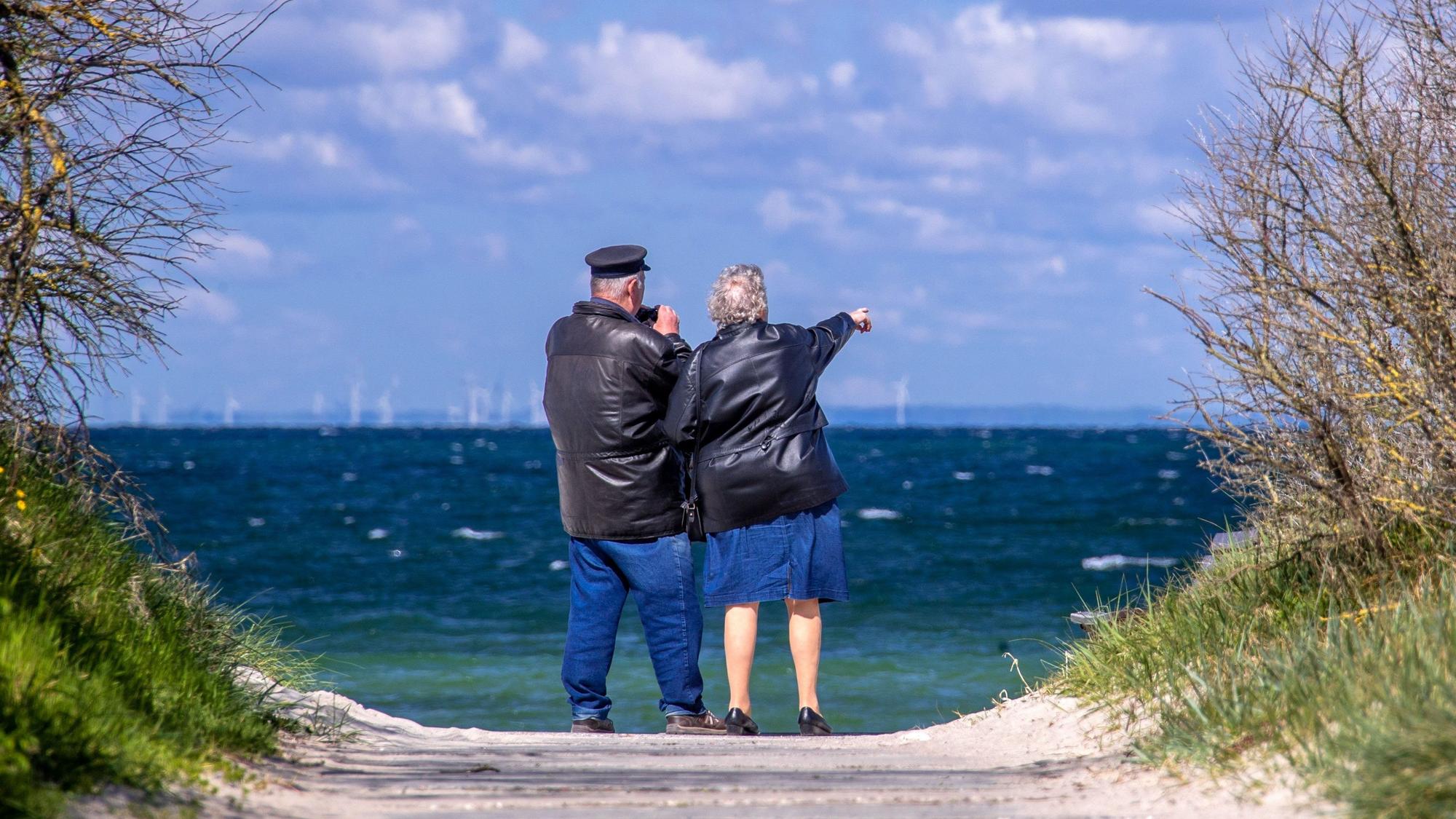 Ein Rentnerpaar steht am ansonsten menschenleeren Strand und schaut aufs Meer. (Archivbild)