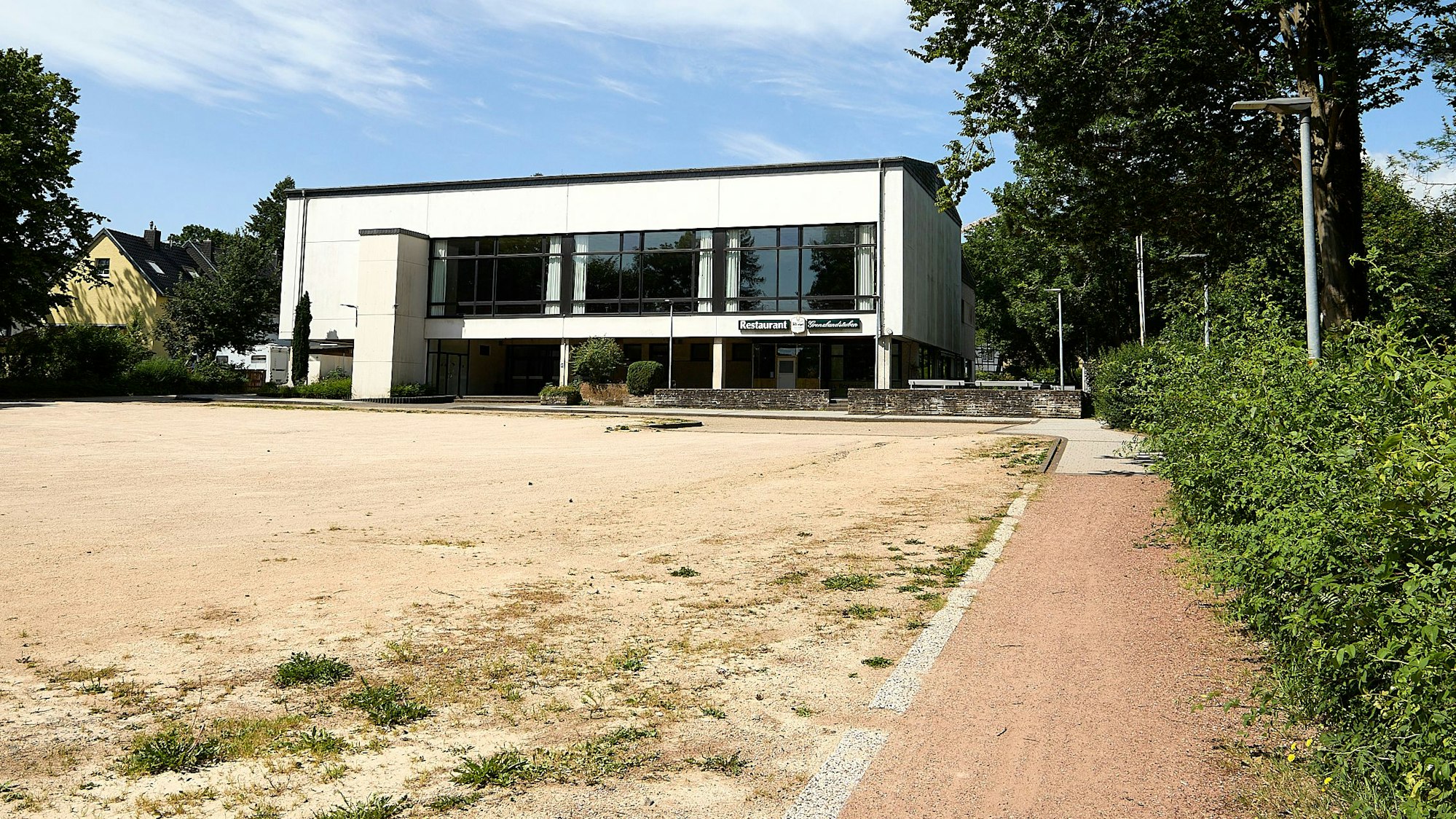 Im Vordergrund ist ein geschotterter Parkplatz, im Hintergrind die Grenzlandhalle in Hellenthal.