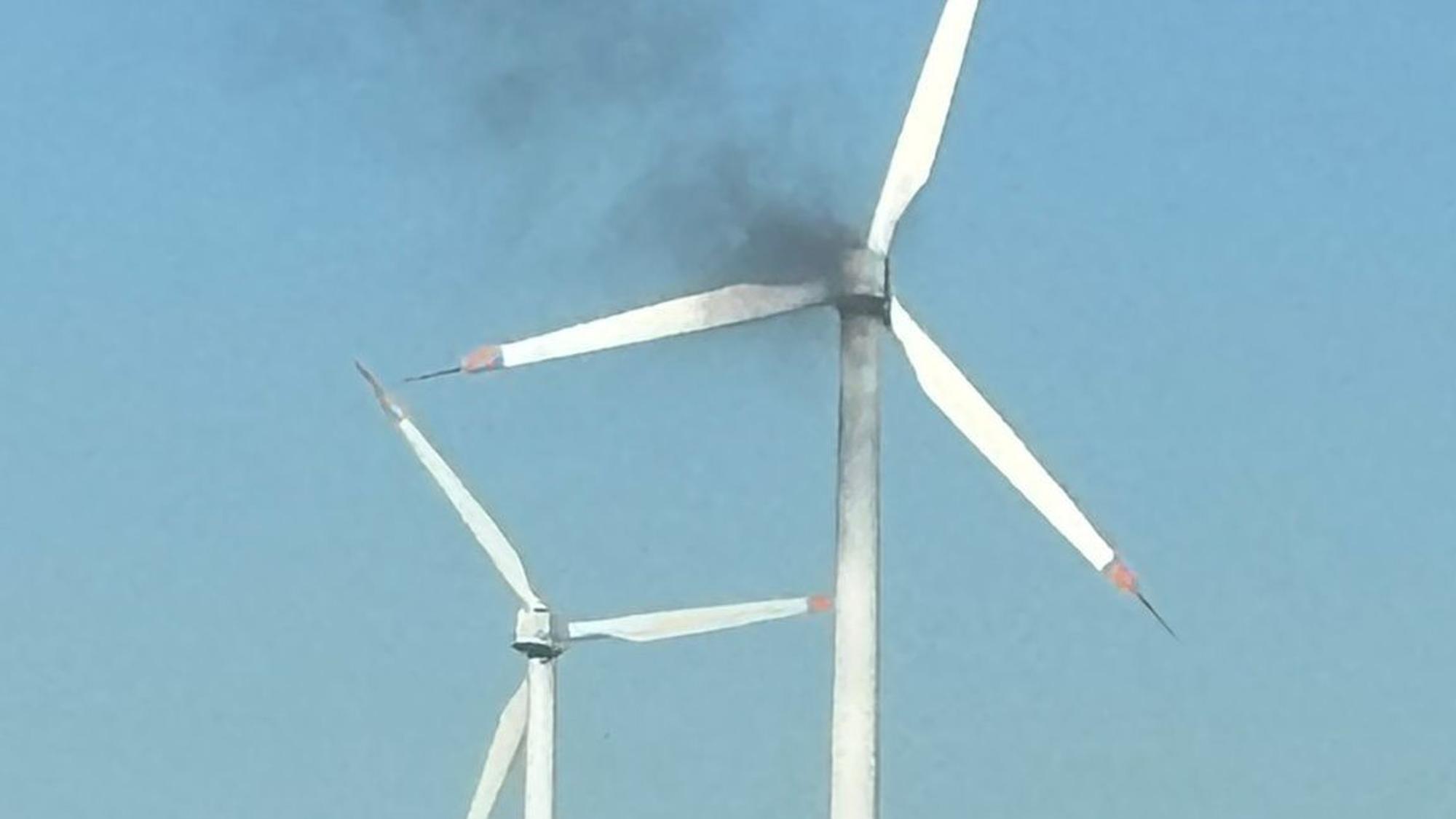 Das Bild zeigt zwei Windkraftanlagen. An einer steigt schwarzer Qualm empor.