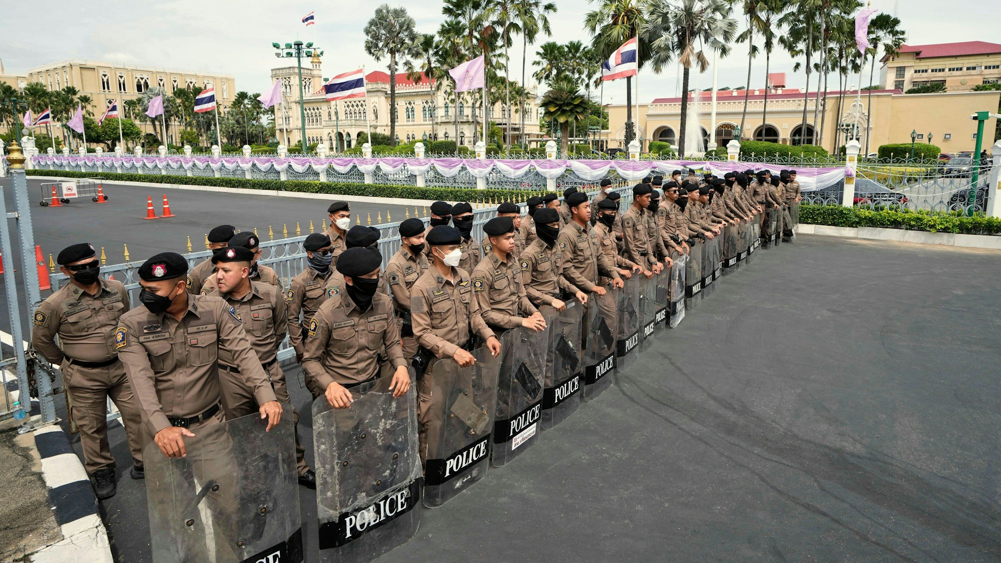 Thailändische Polizisten halten Schilde, als sich regierungskritische Demonstranten vor dem Regierungsgebäude versammeln.