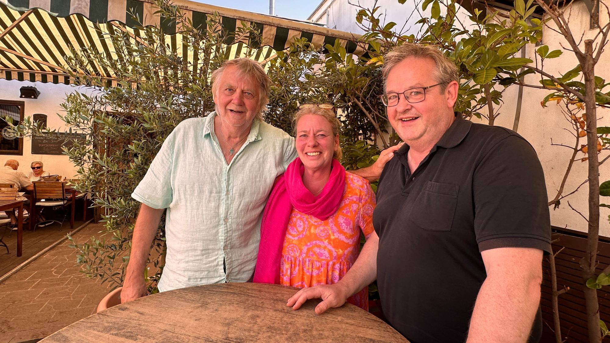 Zwei Männer und eine Frau stehen an einem Stehtisch in einem Biergarten.