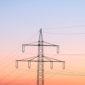 Ein Strommast ist bei Sonnenaufgang als Silhouette zu sehen.