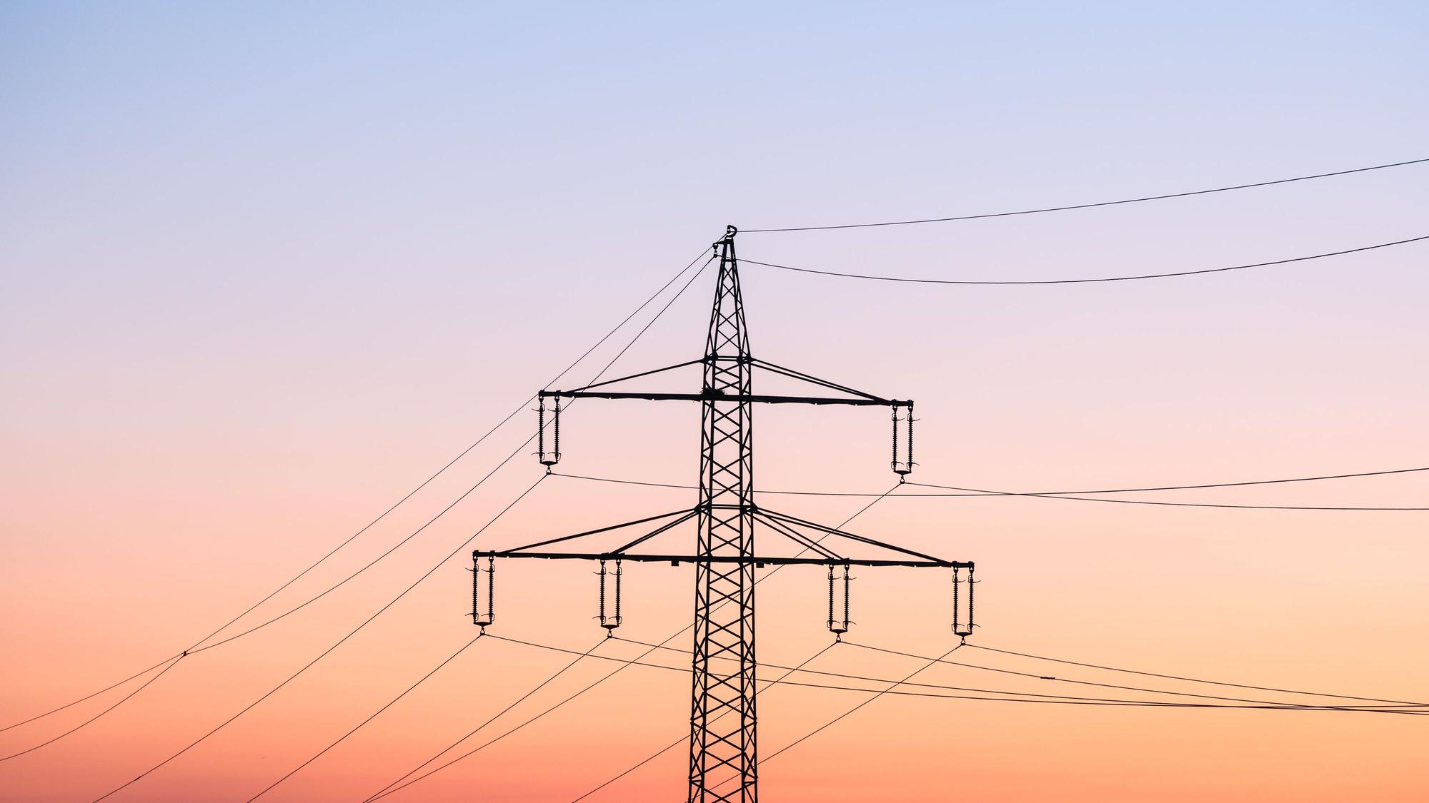 Ein Strommast ist bei Sonnenaufgang als Silhouette zu sehen.