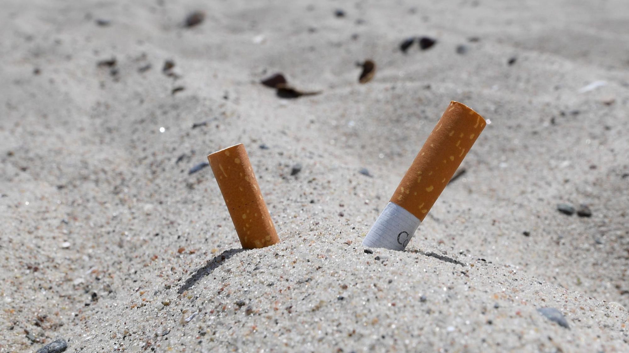 Zigarettenkippen stecken im Sand.