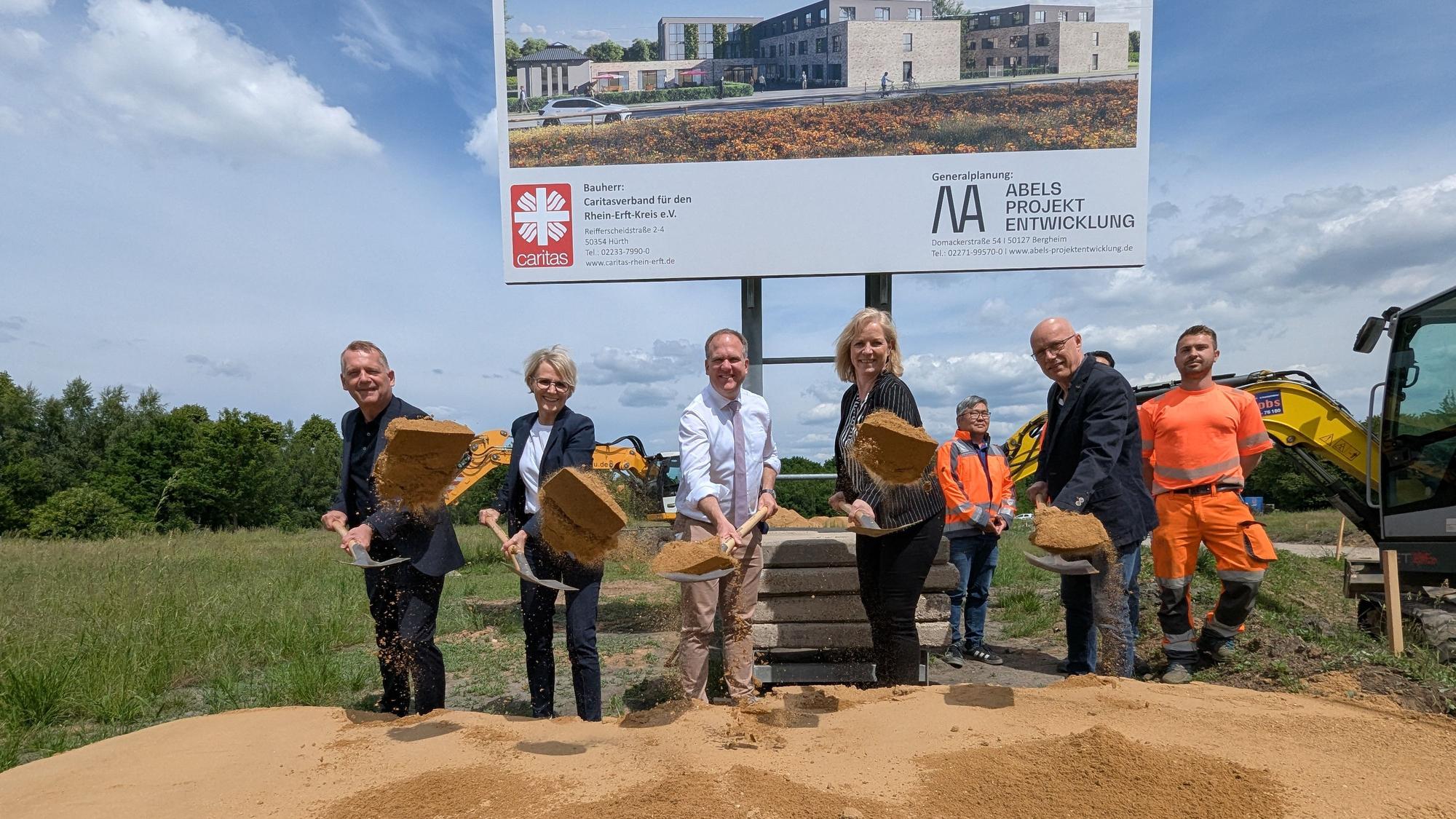 Das Foto zeigt eine Gruppe von Menschen mit Spaten hinter einem Sandhaufen.