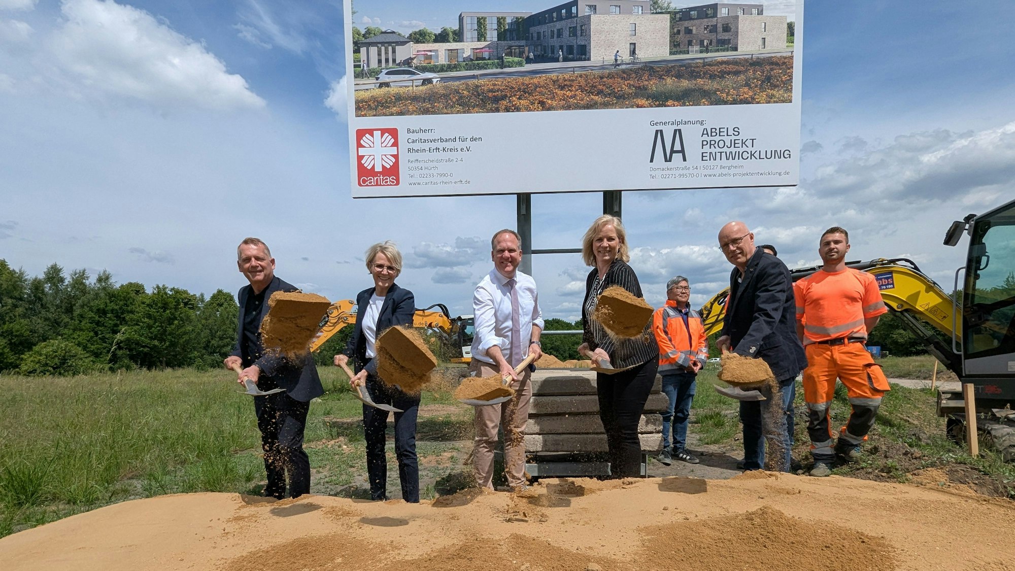 Das Foto zeigt eine Gruppe von Menschen mit Spaten hinter einem Sandhaufen.