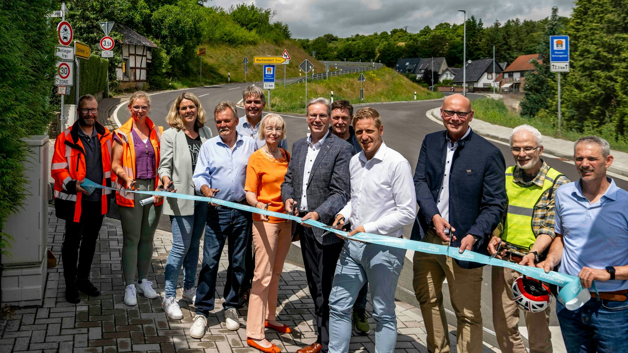 Das Bild zeigt zahlreiche Menschen, die symbolisch ein Band durchschneiden wollen.