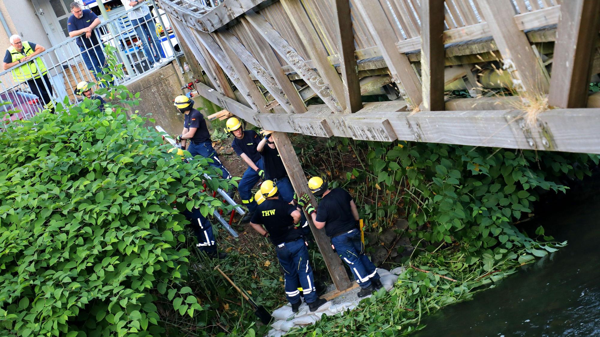THW-Helfer stützen eine einsturzgefährdete Brücke mit einem Holzbalken ab.