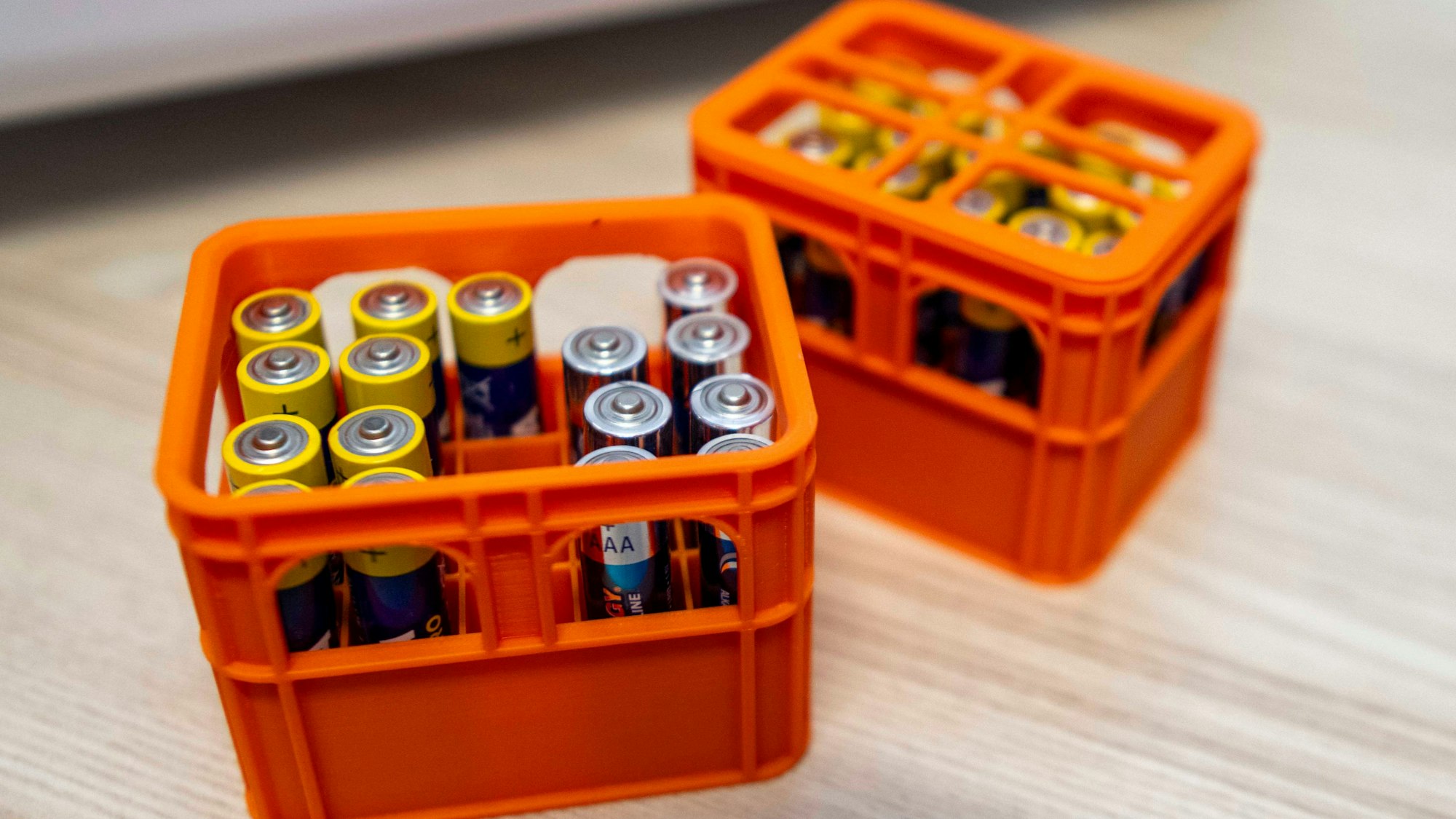 Das Bild zeigt das Endprodukt des 3D-Druckers. Es sind kleine, orange Boxen, die an Bierkästen erinnern. Dort stehen kleine Batterien drin.
