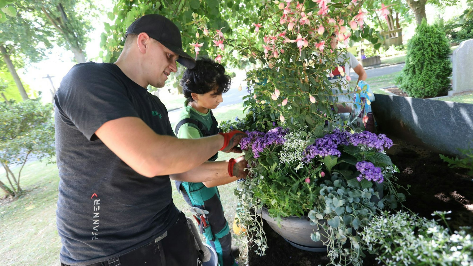 Ein Mann und eine Frau gestalten im Schatten eines Baumes zwei Pflanzschalen.