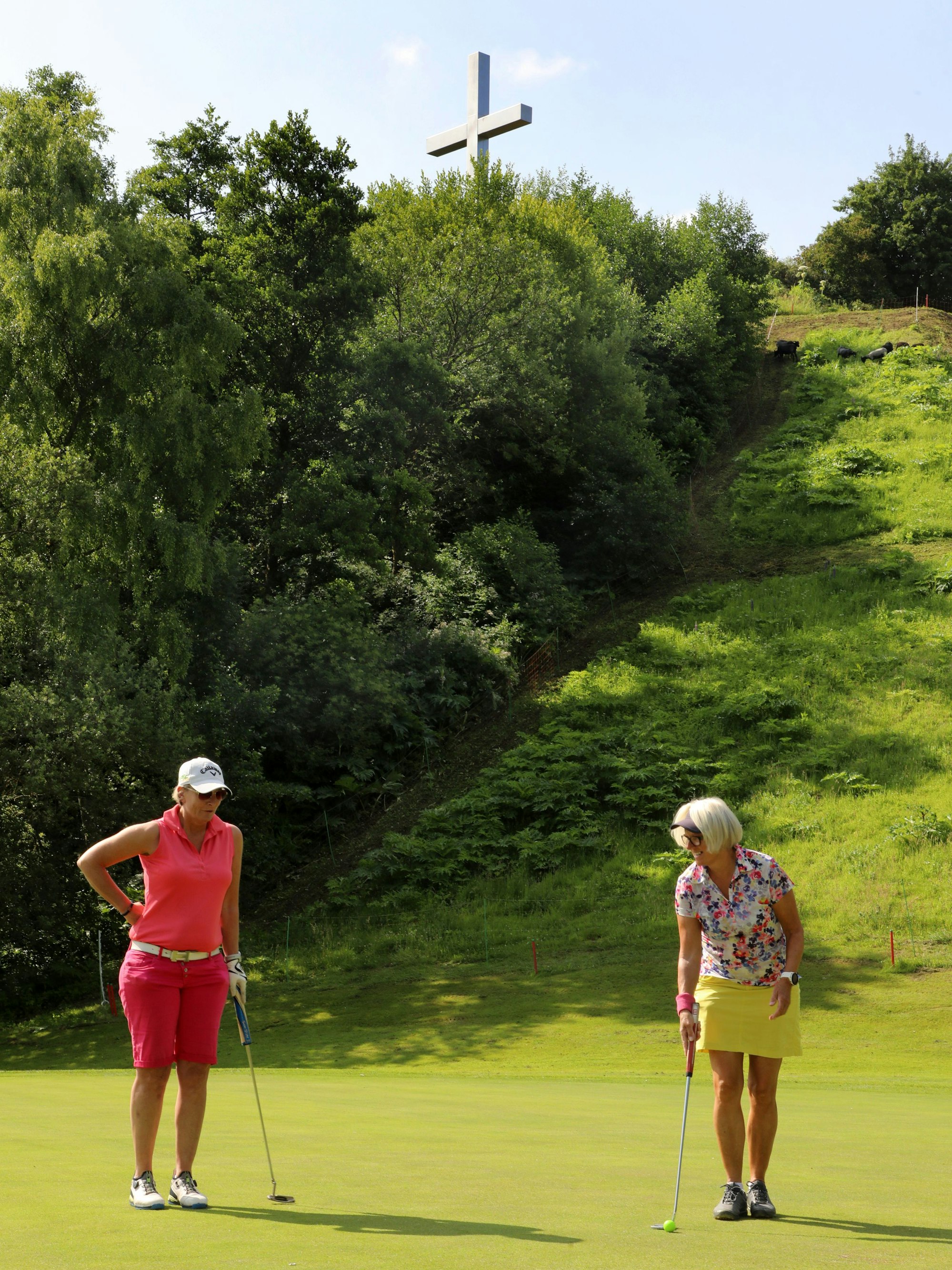 Zwei Golferinnen spielen auf dem Golfplatz „Der Lüderic“h. Im Hintergrund ist das Barbarakreuz zu sehen.