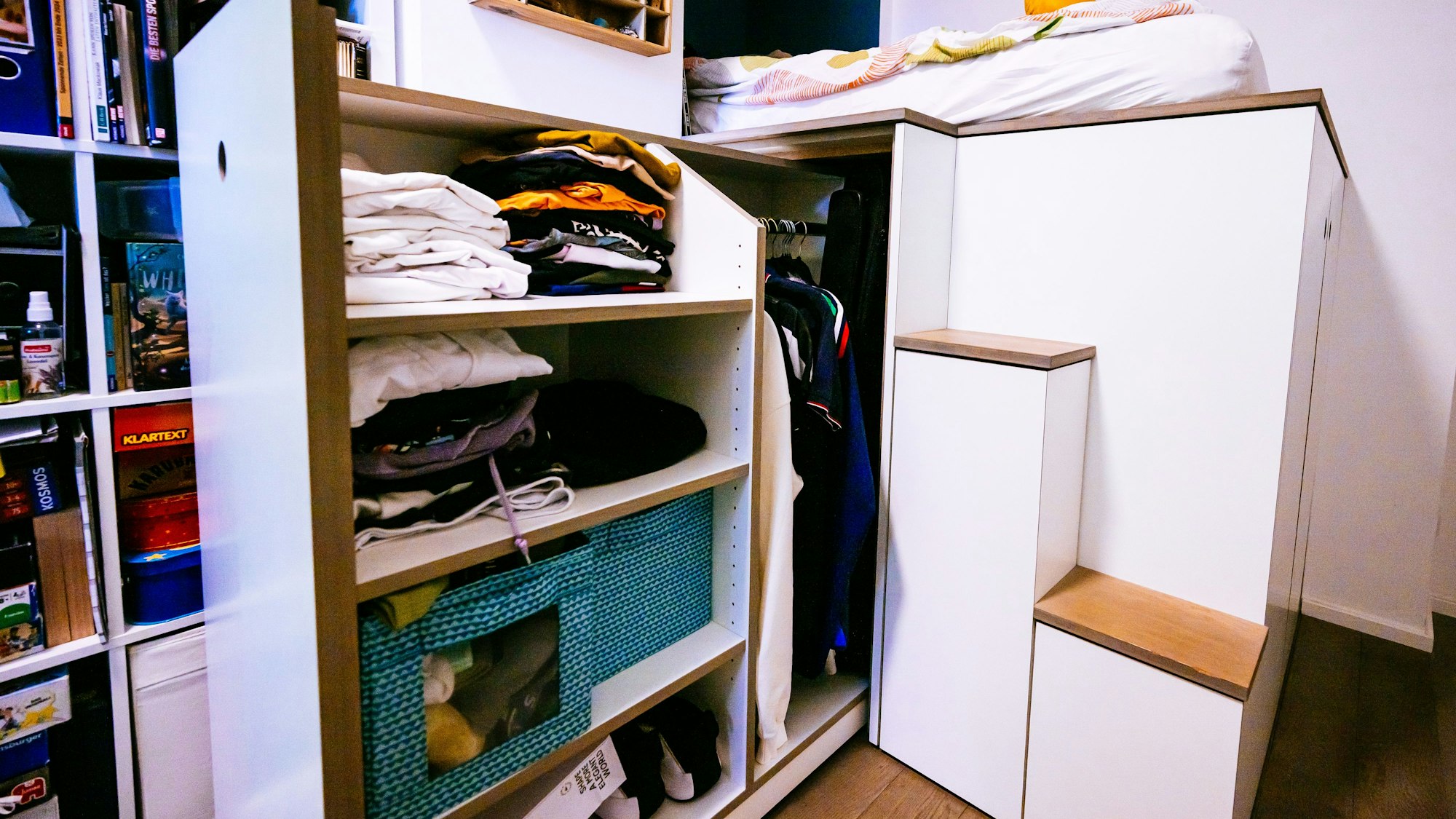 Mit dem ausziehbaren Kleiderschrank wird der Stauraum unter dem Bett-Podest genutzt.