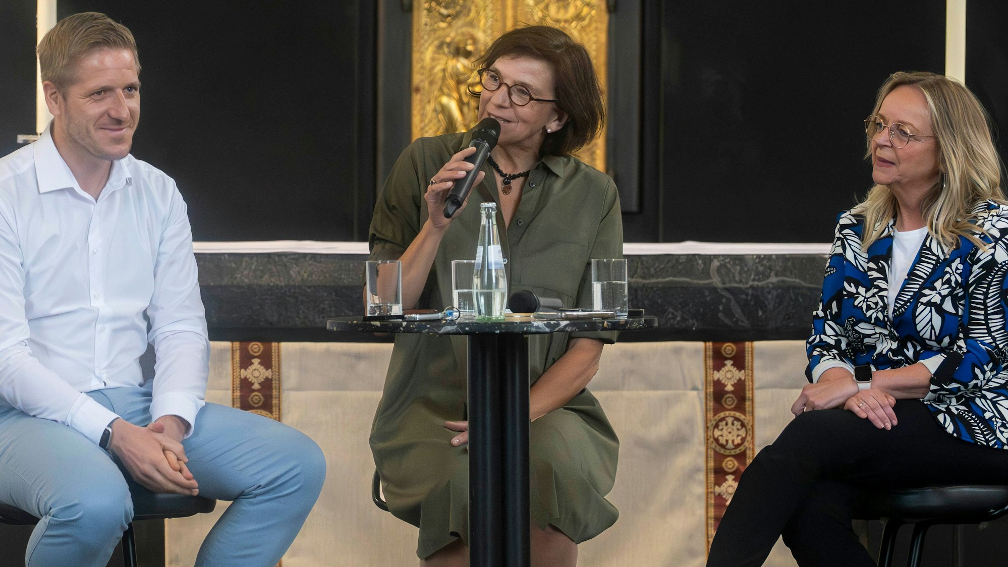 Das Bild zeigt einen Moment der Talkrunde. Marianne Komp hält ein Mikrofon in der Hand, die beiden Landratskandidaten sitzen auf Stühlen und lauschen.