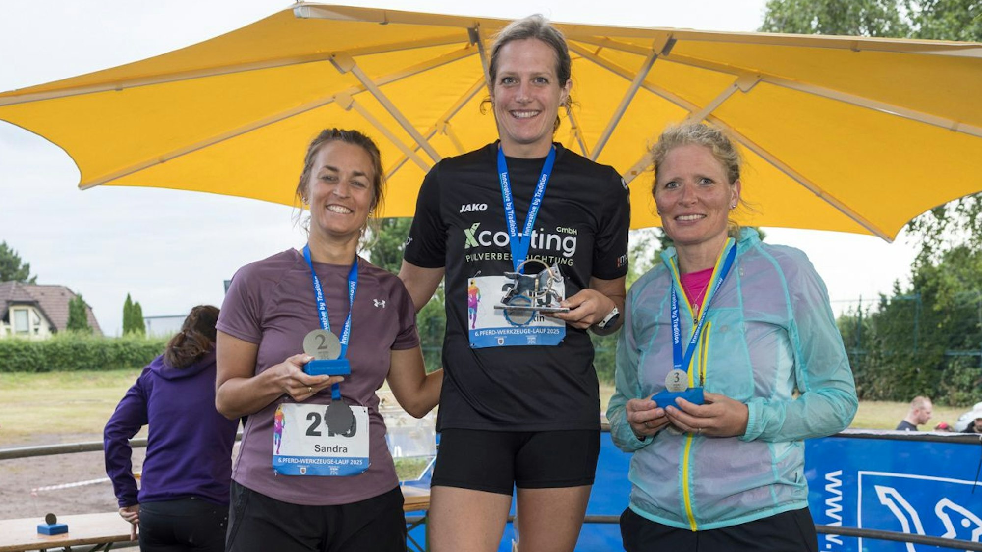 Drei Frauen stehen auf einem Siegerpodest.