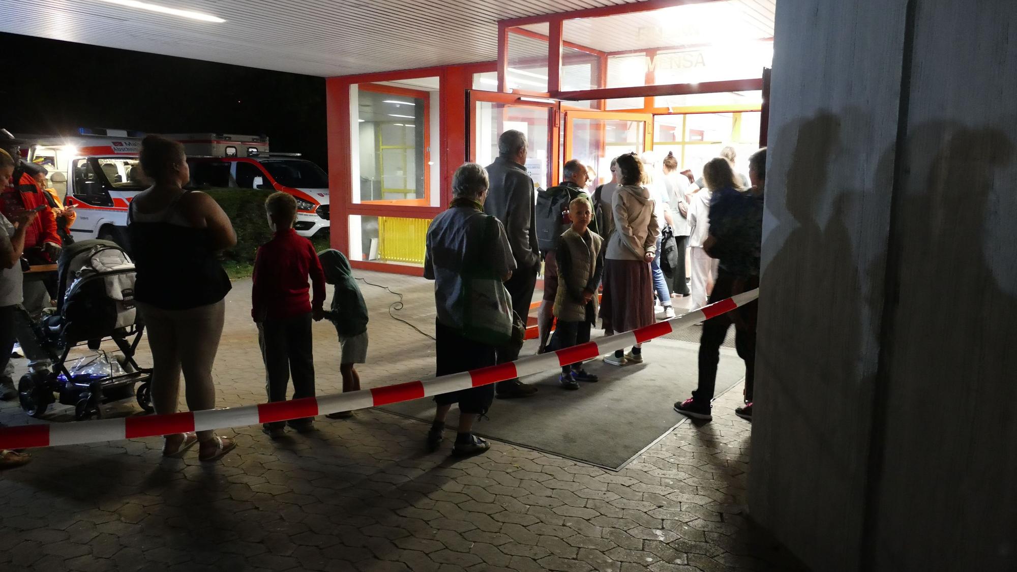 Vor der Turnhalle am Schulzentrum Neuenhof stehen Menschen Schlange, um sich registrieren zu lassen.