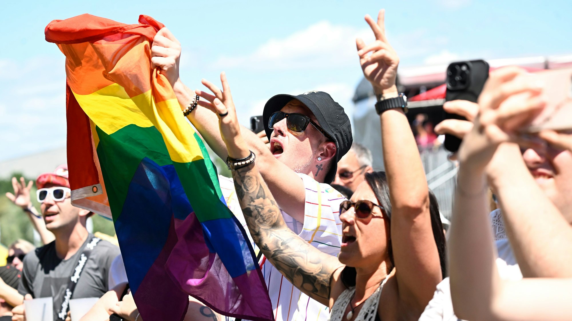 Konzertpublikum mit einer Regenbogenflagge im Sonnenschein.