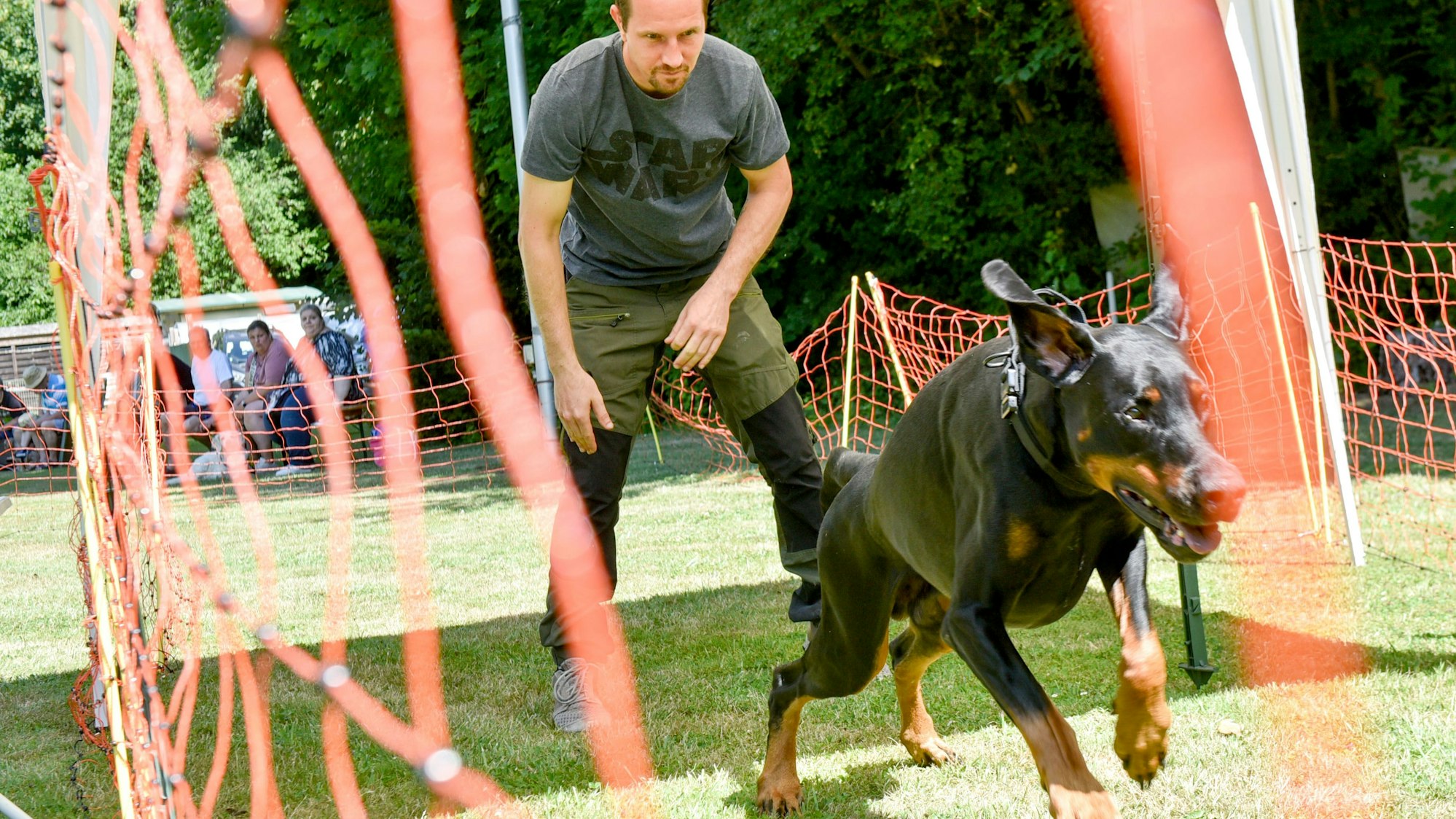 Ein Hund rennt, sein Herrchen steht dahinter.