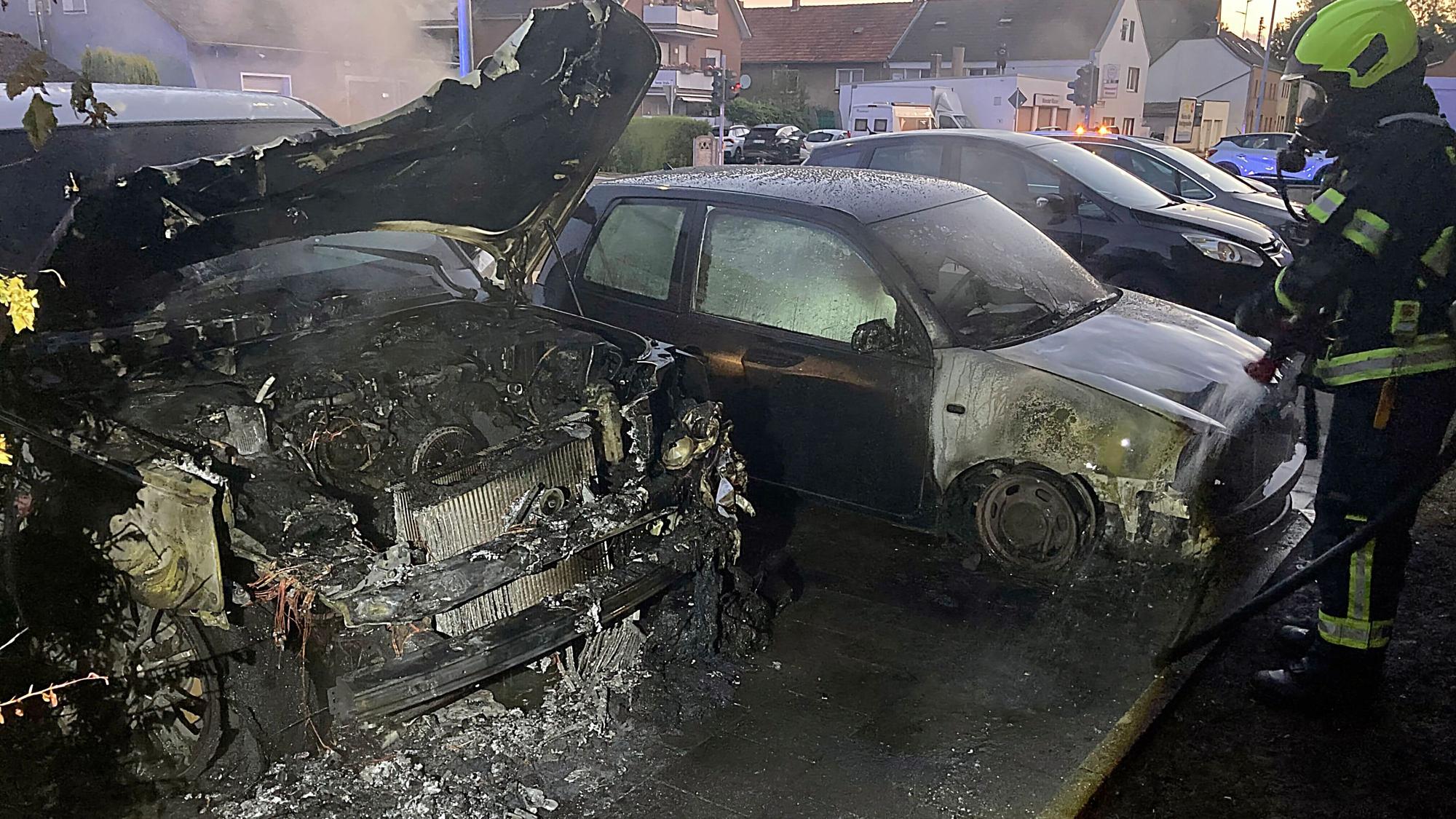 Auf dem Bild sind zwei ausgebrannte Autos und ein Feuerwehrmann zu sehen.