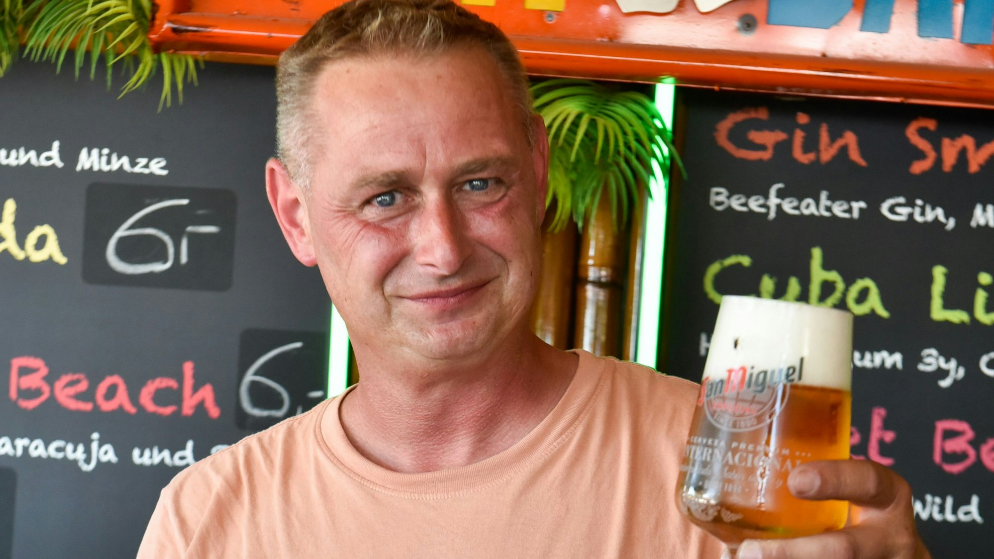 Auf dem Bild ist ein Mann zu sehen, der ein volles Bierglas in die Kamera hält.