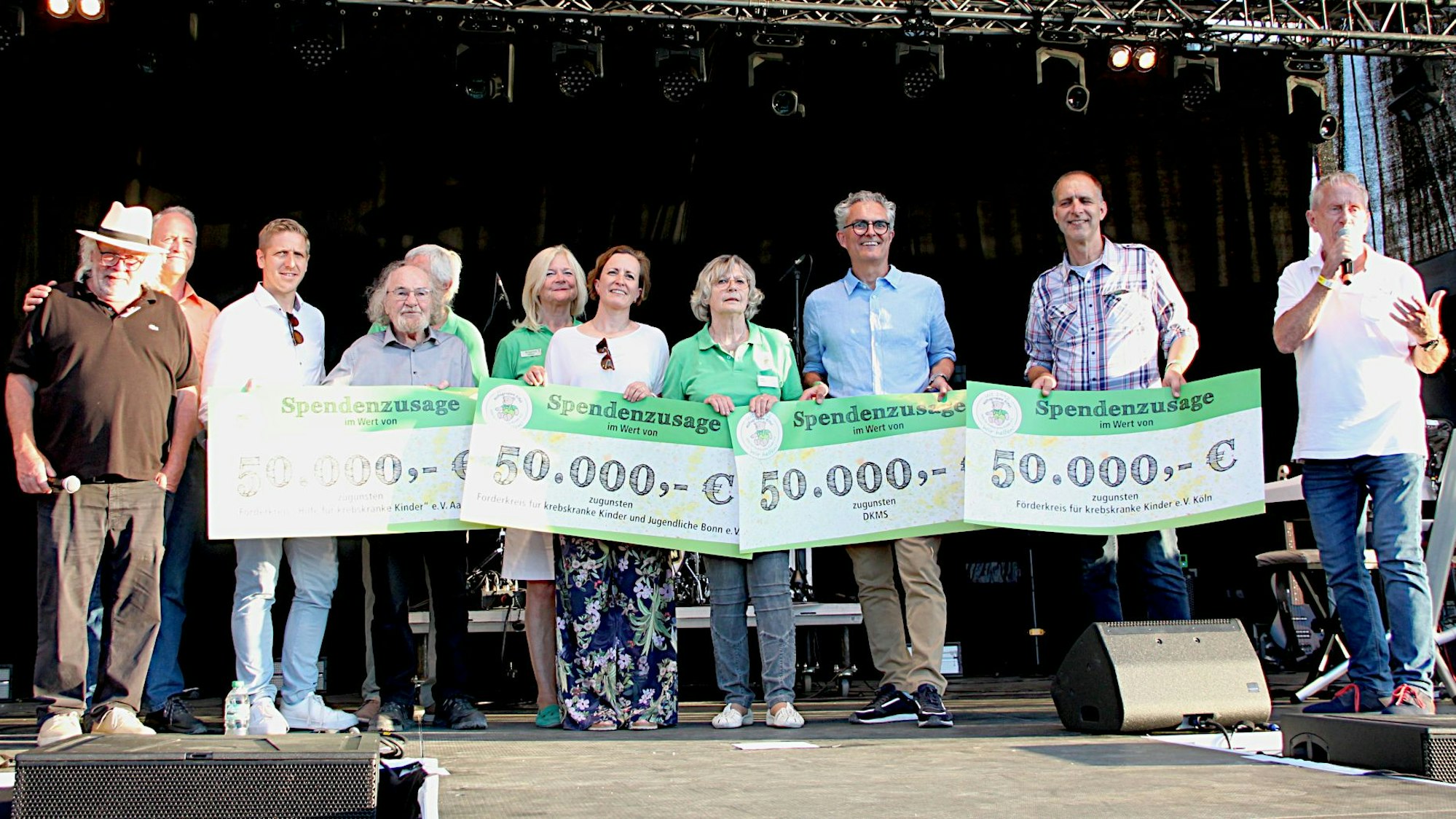 Die Vertreter verschiedener Hilfsorganisationen stehen mit überdimensionierten Spenden-Schecks auf einer Veranstaltungsbühne.