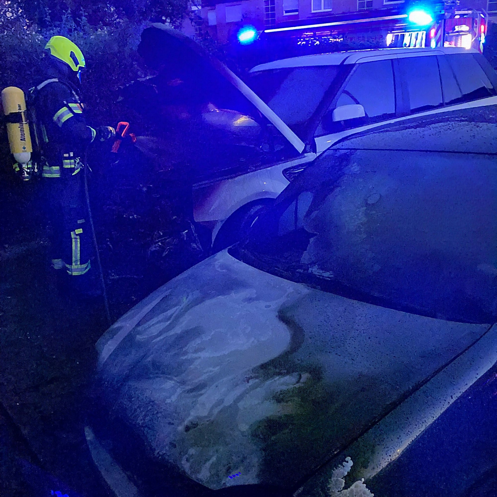 Auf dem Bild ist ein ausgebranntes Auto und ein Feuerwehrmann zu sehen.