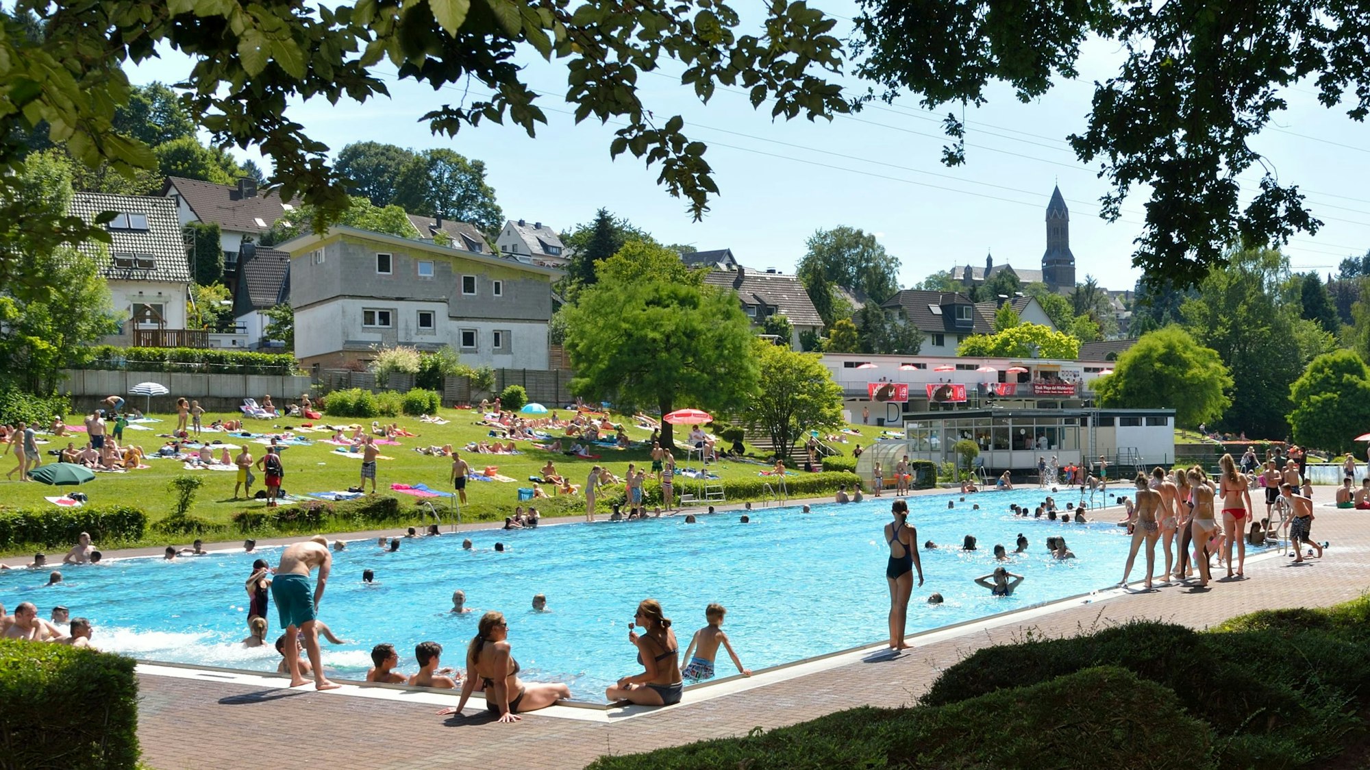 Verschiedene Menschen schwimmen und baden in einem Wasserbecken im Freibad Milchborntal.