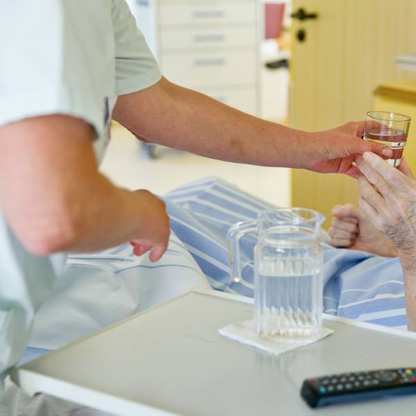 Eine Krankenpflegerin reicht einem Patienten ein Glas Wasser.